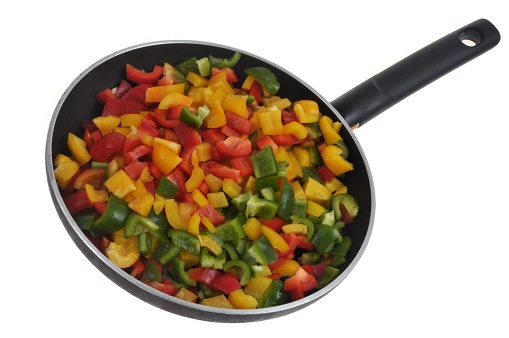 Frying pan on a white background with cut pieces of peppers of different colors