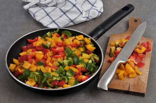 Pan with pieces of peppers of different colors cut with a cutting board and a knife