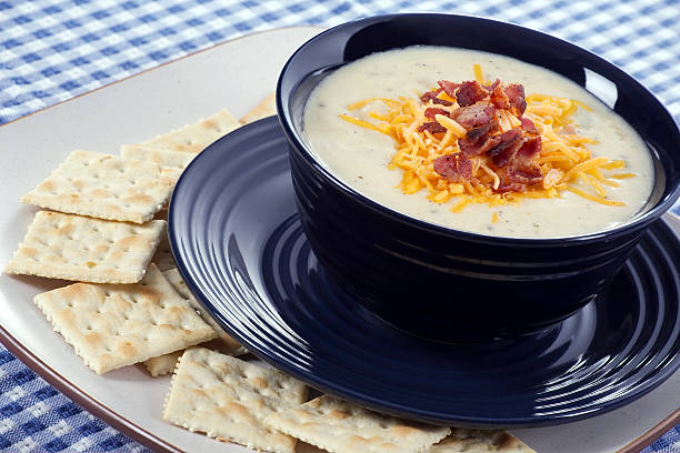 Baked potato soup in a bowl surrounded by soda crackers stock photo