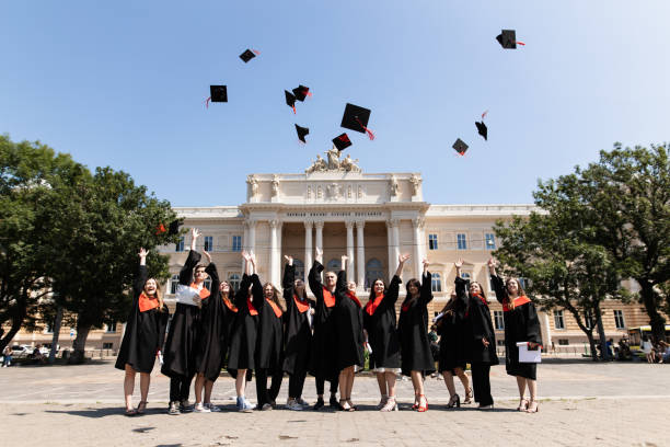 A group of cheerful students in graduation robes throws up their square academic caps as a symbol of university graduation