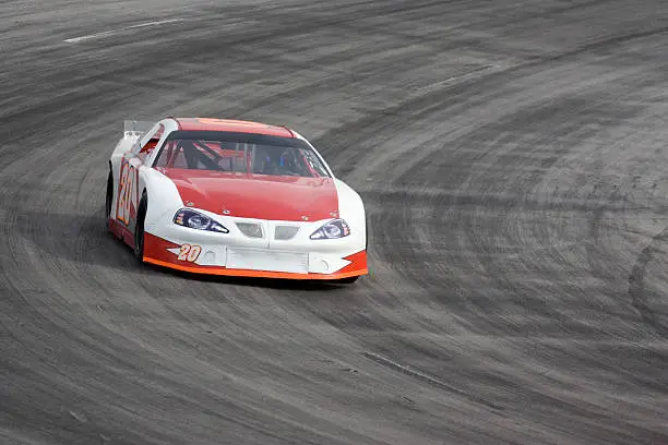 A late model stock car racing on an oval track. Room for copy.