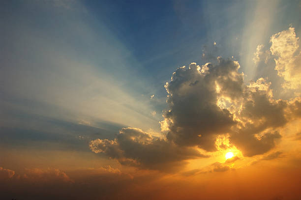 The sun setting with clouds forming around it stock photo