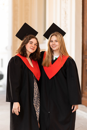 In this heartwarming scene, two cheerful graduates, dressed in their graduation robes, radiate joy and excitement as they celebrate their academic accomplishments. Their faces light up with happiness and pride, reflecting the culmination of their hard work and dedication throughout their educational journey.