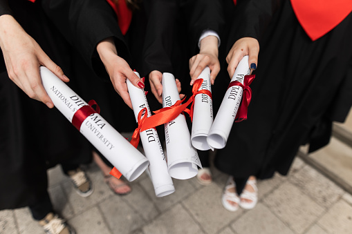 A group of joyful students, dressed in their graduation robes, come together to celebrate their friendship and hard work during their time at the university. They hold their scrolls of education certificates, representing their academic achievements, with beaming smiles of pride and happiness.