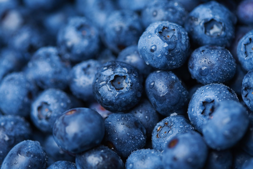 Tasty fresh blueberries with green leaves on light blue background, flat lay. Space for text