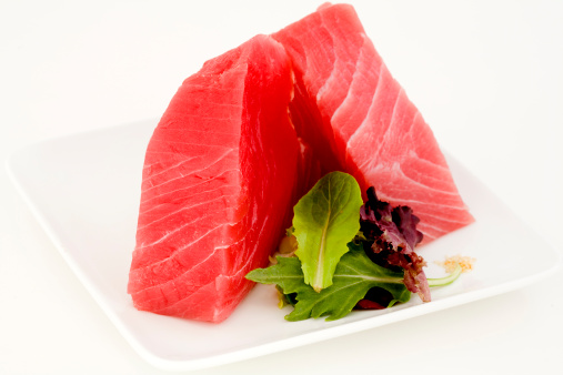 Fillets of Ahi with salad greens on a white plate.