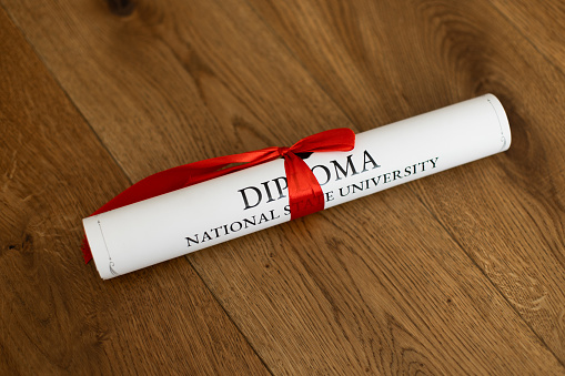A parchment diploma scroll, rolled up with red ribbon laid at an oblique angle.  Processed to give a vintage or retro appearance.
