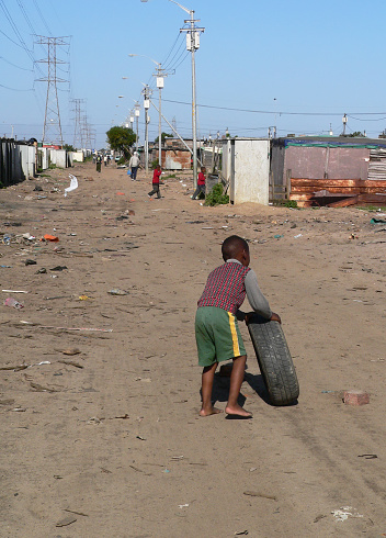 Little boy playing with a car tyre in a squatter camp situated about 1km from the N1 Gateway. Housing project which is under much critisism. Langa, Cape Town, South Africa.