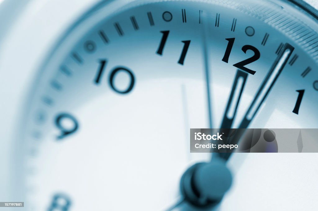 Clock Face Just Past 12 O'Clock A blue toned desaturated close up macro image part of a plain, white clock face from 8 to 1, showing a time of two minutes past twelve, with a second hand. The image is shot with a very shallow depth of field with focus on the clock hands.  Clock Stock Photo