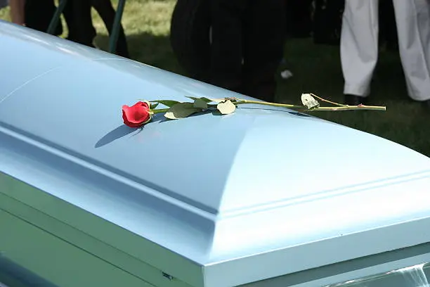 Casket with a single red rose on top of it.