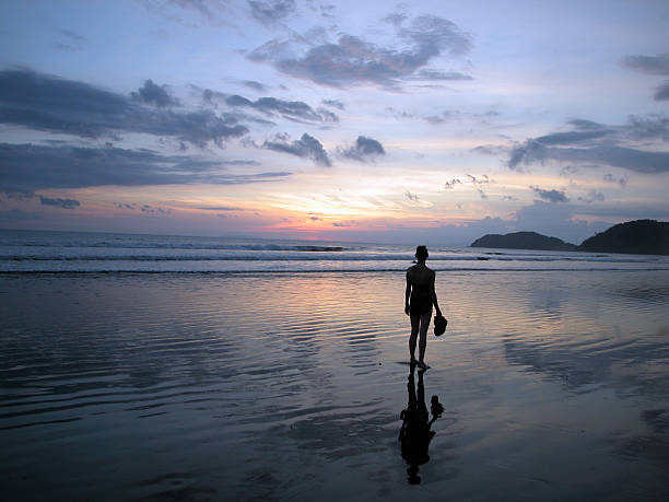 silhueta de mulher caminhando na praia tropical ao pôr do sol - andando em água - fotografias e filmes do acervo