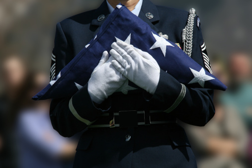 Closeup of woman wearing black at outdoor funeral ceremony clasping hands behind back, copy space