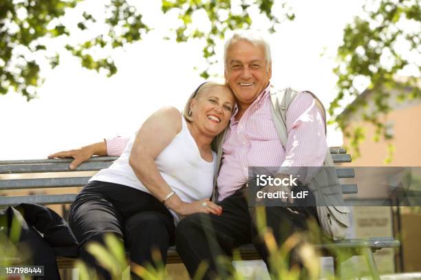 Feliz Pareja Senior Sentado En Un Banco En El Parque Foto de stock y más banco de imágenes de 60-64 años