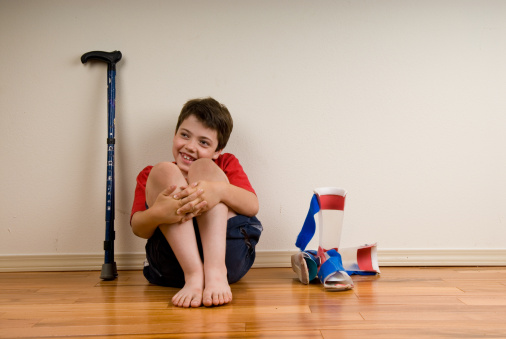 A disabled boy sits on the floor waiting to put on his leg braces