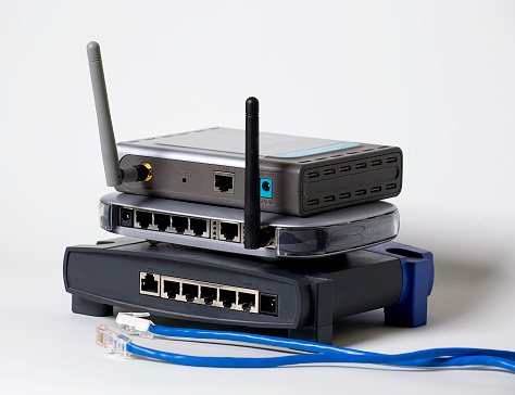 A stack of three wireless computer routers against a white background.  Ethernet cable is laying by the equipment.