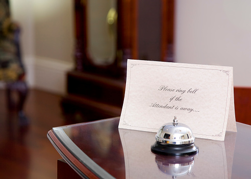 A front desk at a bed & breakfast type hotel.  A bell is on the desk with a sign reading \