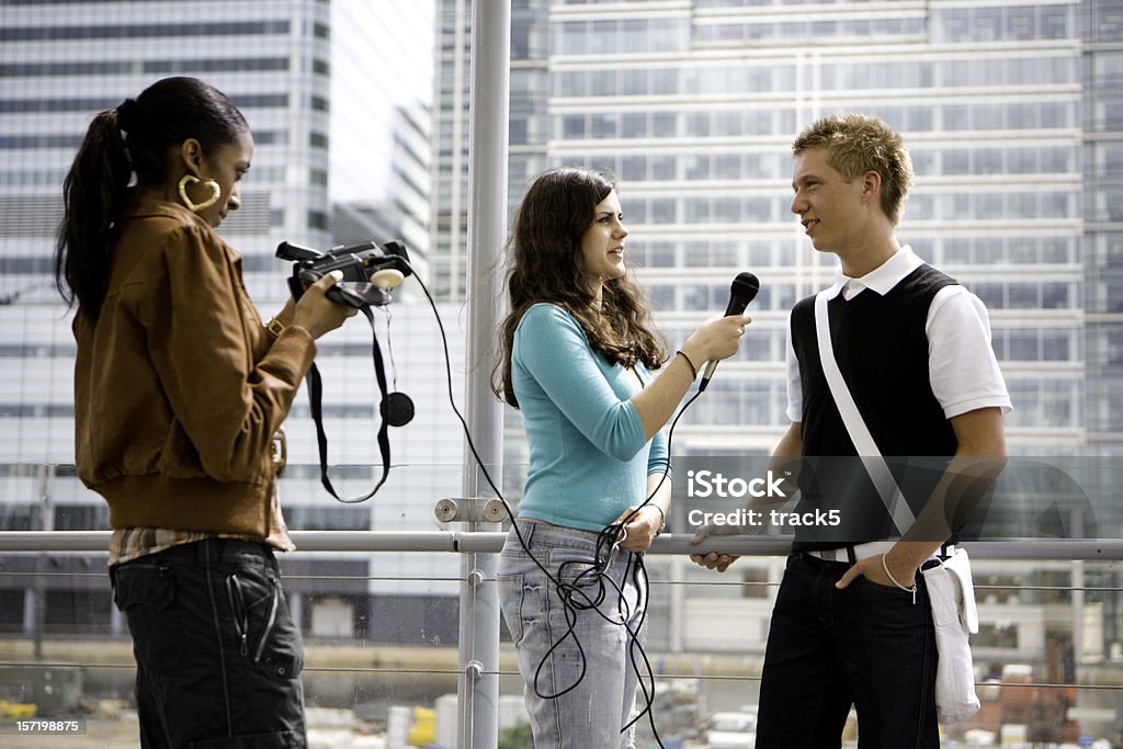 Un hombre joven adolescente en una entrevista por dos jóvenes mujeres - Foto de stock de Entrevista con medio de comunicación libre de derechos
