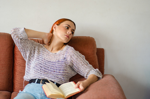 Portrait of Young woman relaxing while she is reading a book in her living room