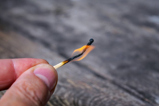 istock Men's fingers hold a burning match on a blurred background. 1572012422