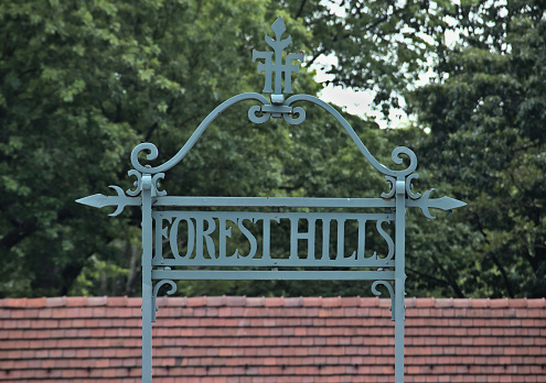 forest hills sign on the train platform (railway station in queens, long island) rail, railroad commute, travel, transportation, rails, metro, urban, painted metal sign w. trees and roof background