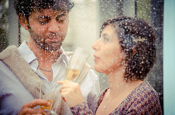 istock Young couple in love behind a wet window drinking champagne 157204929