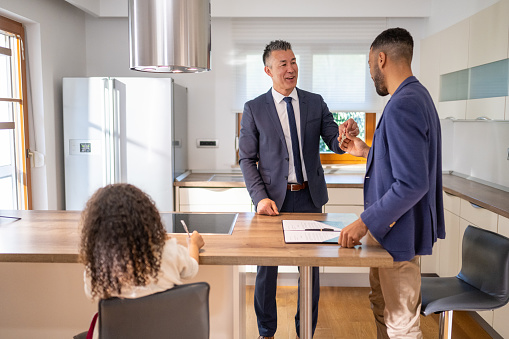 Real estate agent giving key for new house to customer in kitchen.