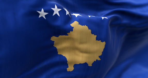 National flag of Kosovo waving in the wind on a clear day. Blue with a yellow map of Kosovo and six white stars above it. 3d illustration render. Selective focus. Fluttering fabric background
