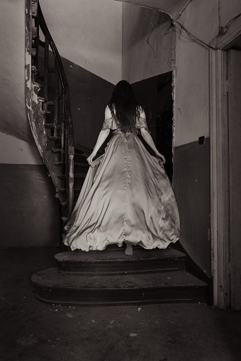 Young and attractive woman running against old stairs from an abandoned house.