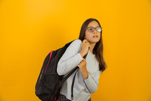 Little cute smart girl in glasses with backpack on her shoulders looks tired.