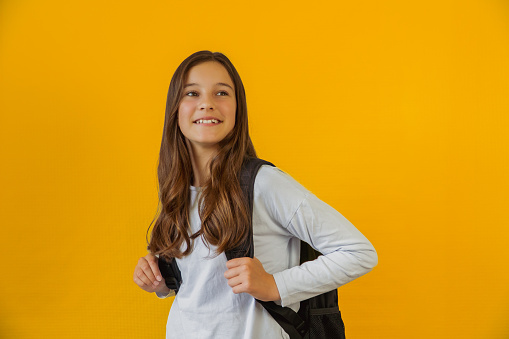 Portrait of little cute girl schoolgirl with backpack yellow background