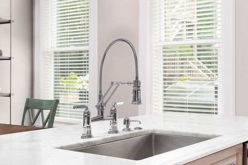 A kitchen sink detail with a chrome faucet, white marble countertop, and stainless steel sink basin.