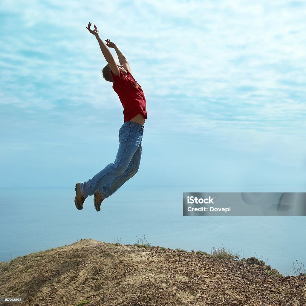 Man jumping cliff Man jumping cliff against sea and mountain with blue sky Activity Stock Photo