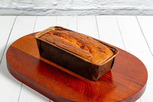 An English cake in a baking dish on a wooden board and a white wooden table. Selective focus