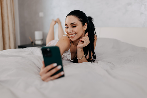 Enjoying a moment of relaxation, the woman snaps a selfie in bed, ready to embrace the day with enthusiasm and joy