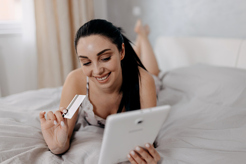 Maximizing the potential of technology, the woman enjoys a seamless online shopping spree using her digital tablet while resting in bed