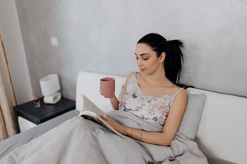Engaging her mind with the world of literature and savoring the taste of her coffee, the woman starts her day on a positive note, nestled in her bed