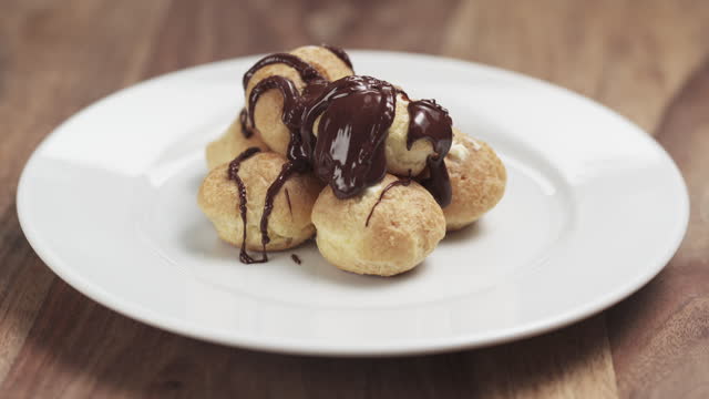 Slow motion fly out shot of profiteroles with fine dark chocolate on plate