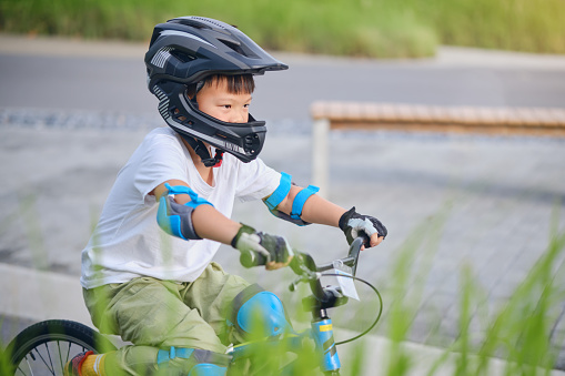 Cute little 7 years old school boy child in safety helmet wearing knee pads, elbow pads and cycling gloves riding a bike on nature, Kid cycling, playing outside at park, Fun exercise for kids
