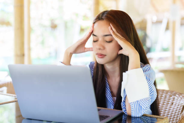 istock Asian woman with stressed back working in front of one laptop computer on front desk. with a stern expression, rubbing his head with his hands having a headache from work 1572207780