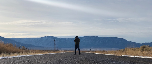 Photographer looks down an open road with mountain range in distance.