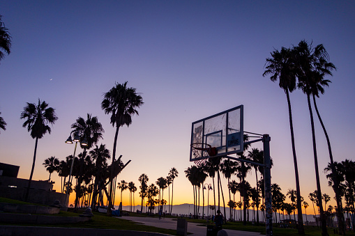 Silhouettes in the colorful sunset sky of palm trees, basketball hoops, and other things at Venice Beach in Los Angeles, California.