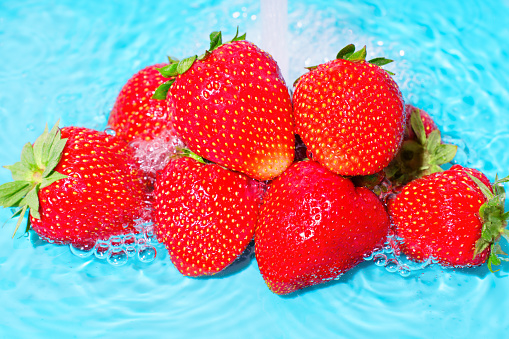 Pile of ripe strawberries being gently cleansed under a refreshing water jet.