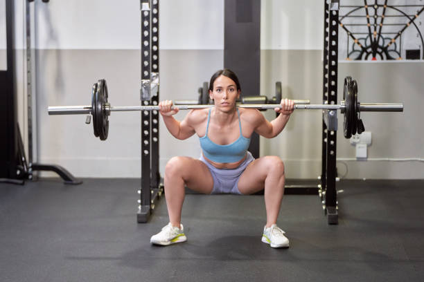 istock A young woman performs a shoulder press with a heavy barbell during her intense training session. 1572243679