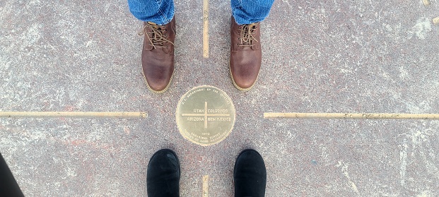 2 sets of booted feet standing at the famous 4 Corners of the USA. The 4 corner states are Colorado, Utah, Arizona and New Mexico where all 4 states meet in one spot.
