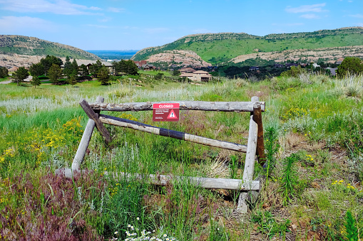Buck fence with Closed Trail sign along hiking trail in mountains, green grass with wildflowers meadow natural landscape. Restricted access due to habitat restoration. Barrier, obstacle concept.