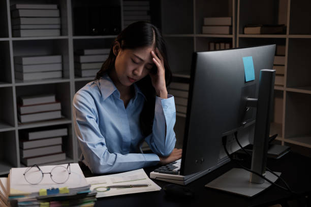 istock Stressful Asian businesswoman having a headache while working overtime at night, feeling tired after a long day at work. 1572295942