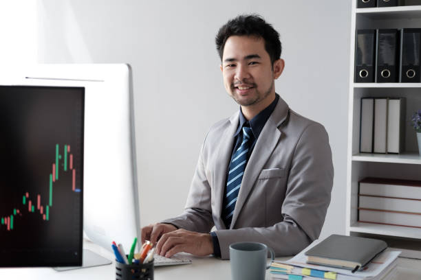 istock Middle aged Asian businessman analyzing investment trending, working on the computer in his office room. 1572302605