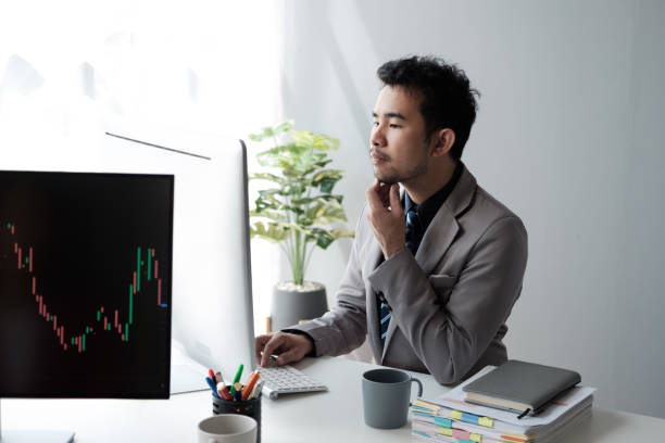 istock Middle aged Asian businessman analyzing investment trending, working on the computer in his office room. 1572303113