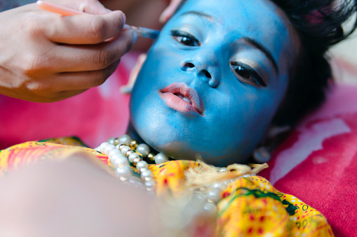 Indian little boy dressed as Lord Krishna and painted his face with blue color for Krishna Janmashtami celebration in India.