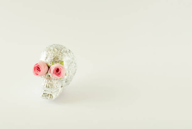 Silver sugar skull with pink roses instead of eyes on the white background with copy space.